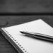 A black and white image of a notepad with a fountain pen lying on top of it
