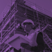 Construction worker wearing a hard hat and safety vest holds a tablet at a scaffolded building site, shown with a purple color overlay.